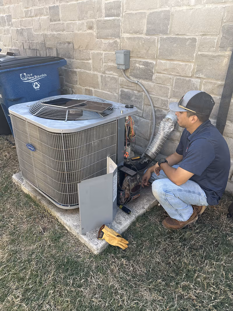 Technician repairing an air conditioning unit outside near a recycling bin