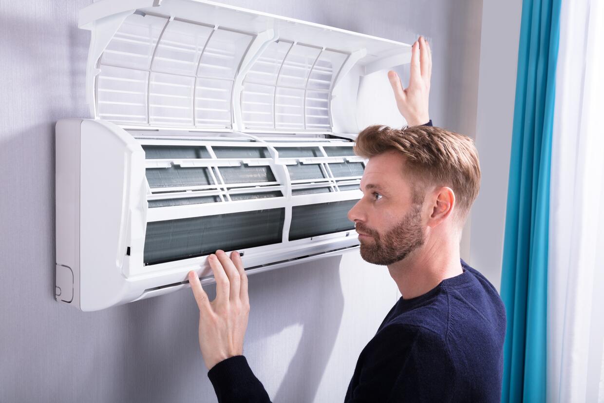 CLOSE-UP OF A YOUNG MAN CHECKING AIR CONDITIONER MOUNTED ON WALL CLOSE-UP OF A YOUNG MAN CHECKING AIR CONDITIONER MOUNTED ON WALL